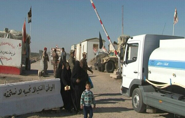رجال شرطة عند نقطة تفتيش أحد مداخل الفلوجة يفتشون السيارات و الأفراد الذين يدخلون الى المدينة لمنع تسلل عناصر داعش إليها. حاجز اسمنتي قرب نقطة تفتيش كتب عليه: "الوطن الذي لا نحبه لا نستحقه". [سيف أحمد/ديارنا]